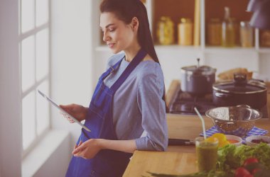 Mutfakta yemek yapmak için tablet bilgisayar kullanan genç bir kadın.