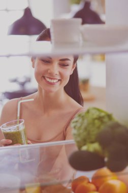 Mutfaktaki masada bir bardak lezzetli, sağlıklı smoothie ile genç bir kadın.
