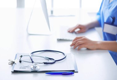 Kadın doktor masada oturuyor ve hastanede dizüstü bilgisayarla çalışıyor.