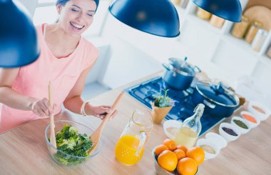 Gülümseyen genç kadın mutfakta taze salata karıştırıyor..