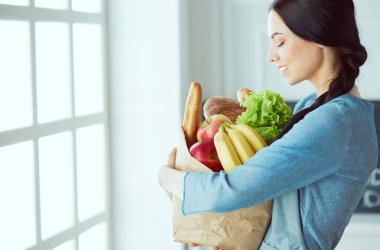 Sebze dolu alışveriş çantasının arkasına saklanan genç bir ev hanımı.