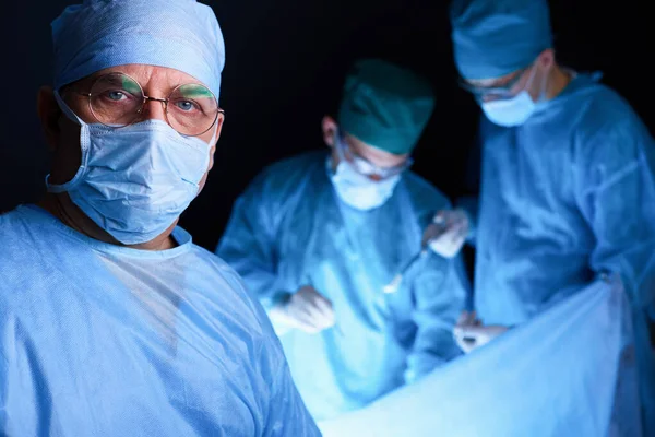 Group of surgeons at work in operating theater toned in blue. Medical team performing operation — Stock Photo, Image