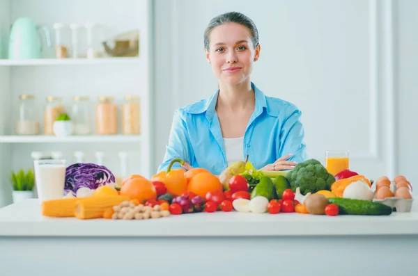 Mujer joven y linda sentada en la mesa llena de frutas y verduras en el interior de madera. — Foto de Stock