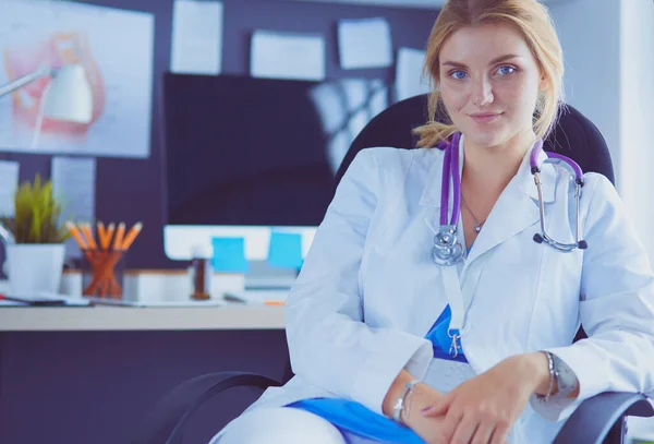Όμορφη νεαρή χαμογελαστή γυναίκα γιατρός κάθεται στο γραφείο — Φωτογραφία Αρχείου