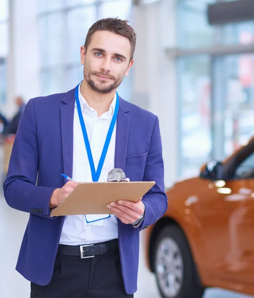 Vendedor fica perto de um carro novo no showroom — Fotografia de Stock