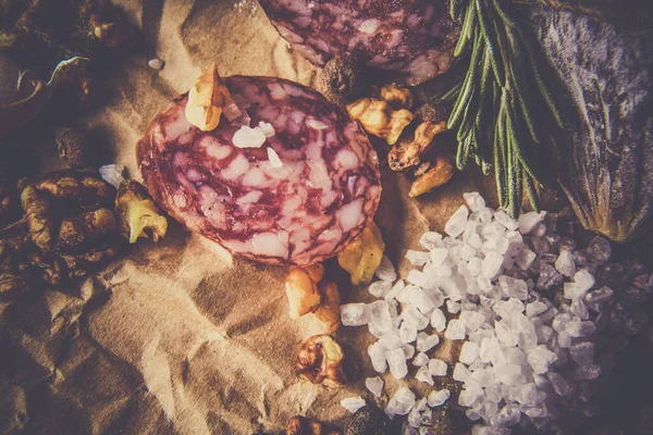 Italiaanse salami met zeezout, rozemarijn, knoflook en noten op papier. Rustieke stijl. Bovenaanzicht. — Stockfoto
