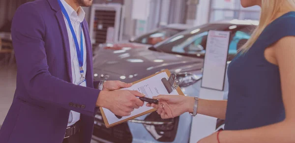 Vendedor de coches vende un coche a cliente feliz en concesionario de coches y las manos sobre las llaves — Foto de Stock