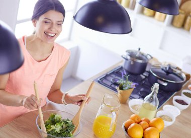 Gülümseyen genç kadın mutfakta taze salata karıştırıyor..