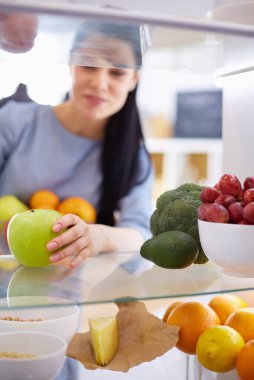 Gülümseyen kadın buzdolabından taze meyve alıyor, sağlıklı yiyecek konsepti.