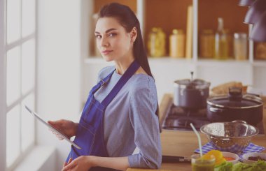 Mutfakta yemek yapmak için tablet bilgisayar kullanan genç bir kadın.