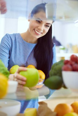 Gülümseyen kadın buzdolabından taze meyve alıyor, sağlıklı yiyecek konsepti.