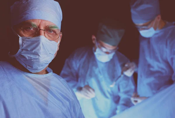 Grupo de cirurgiões no trabalho em sala de operações tonificada em azul. Equipe médica realizando operação — Fotografia de Stock