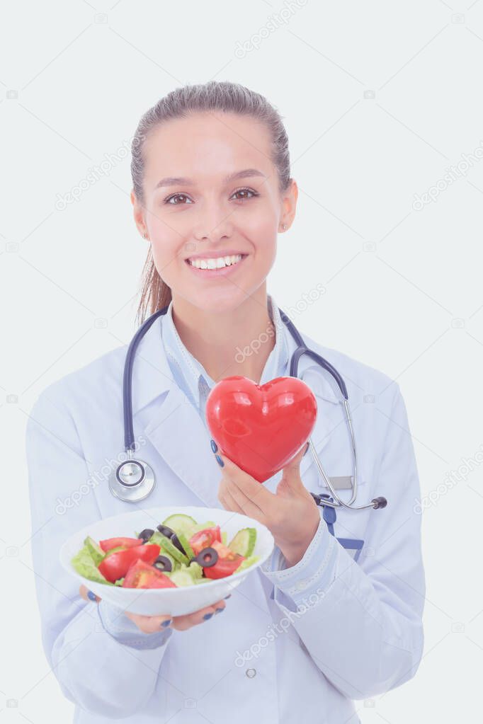 Portrait of a beautiful woman doctor holding a plate with fresh vegetables and red heart. Woman doctors