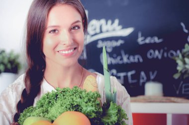 Mutfakta elinde sebzelerle gülümseyen genç bir kadın. Gülümseyen genç kadın