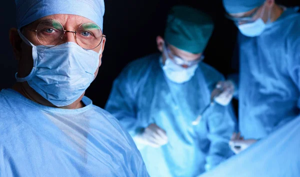 Group of surgeons at work in operating theater toned in blue. Medical team performing operation — Stock Photo, Image