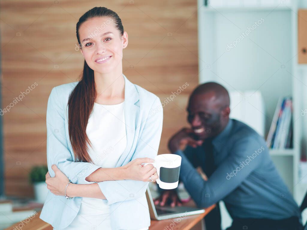 Attractive woman sitting at desk in office having takeaway coffee.