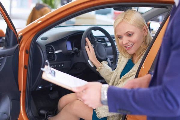 Bela jovem mulher está falando com bonito carro concessionário trabalhador ao escolher um carro na concessionária — Fotografia de Stock