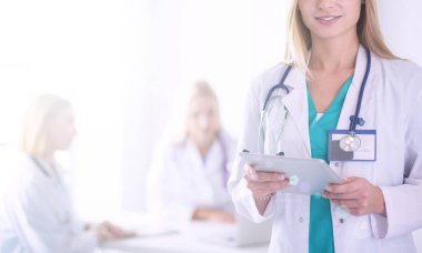 Genç bir kadın doktorun portresi, elinde aipad ile, bir tıp ofisinde.