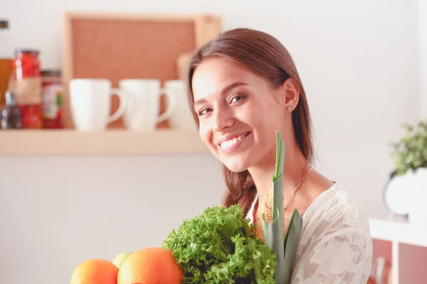 Mutfakta elinde sebzelerle gülümseyen genç bir kadın. Gülümseyen genç kadın — Stok fotoğraf