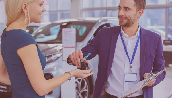 Vendedor de coches vende un coche a cliente feliz en concesionario de coches y las manos sobre las llaves — Foto de Stock