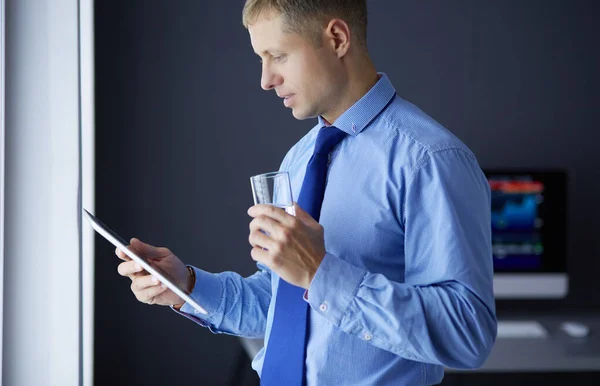 Smiling businessman with touchpad standing at workplace in office — Stock Photo, Image