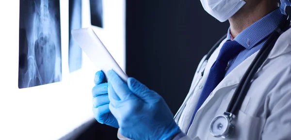Arzt im Krankenhaus sitzt am Schreibtisch und betrachtet Röntgenbilder auf Tablet vor weißem Hintergrund mit Röntgenaufnahmen — Stockfoto