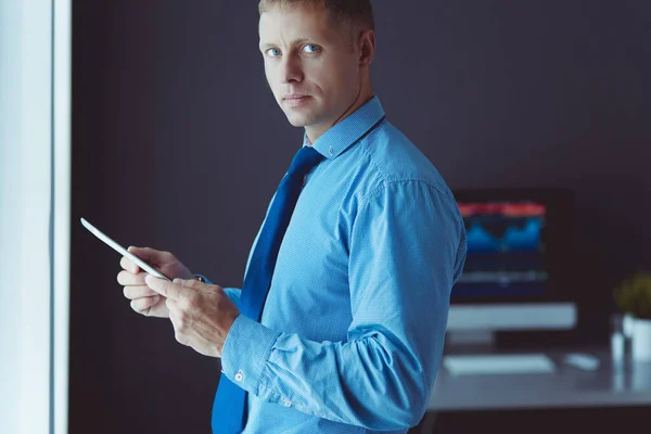 Улыбающийся бизнесмен с тачпадом, стоящий на рабочем месте в офисе — стоковое фото