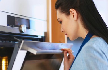Güzel genç bayan pastasının fırında ne yaptığını kontrol ediyor.