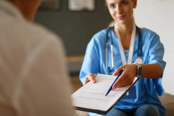 Ärztin hält silbernen Stift in der Hand, der Patientenakte am Klemmbrett füllt — Stockfoto