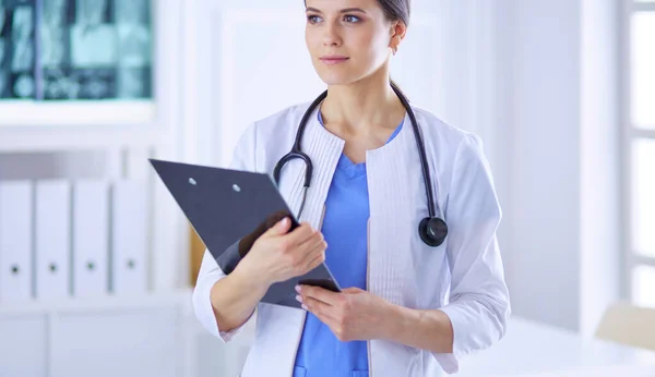 Joven doctora sonriente con estetoscopio sosteniendo una carpeta en el consultorio médico — Foto de Stock