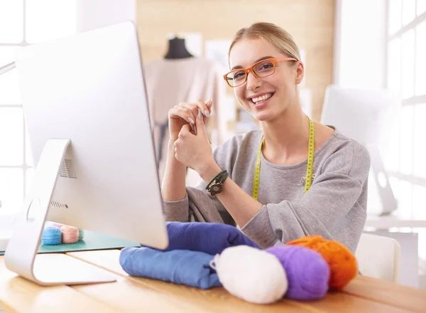一个年轻的设计师妇女使用笔记本电脑和微笑的肖像，衣服挂作为背景 — 图库照片