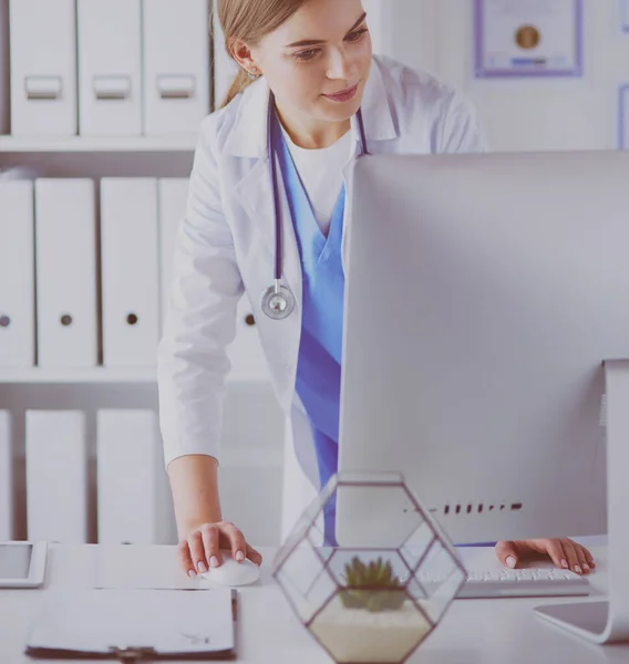 Portrait of female physician using laptop computer while standing near reception desk at clinic or emergency hospital