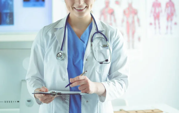 Dokter met een stethoscoop, met een notitieboekje in zijn hand. Close-up van een vrouwelijke arts die een medisch formulier invult aan het klembord terwijl hij recht in het ziekenhuis staat — Stockfoto