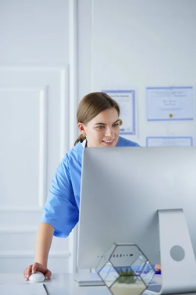 Portrait of female physician filling up medical form while standing near reception desk at clinic or emergency hospital — Stock Photo, Image