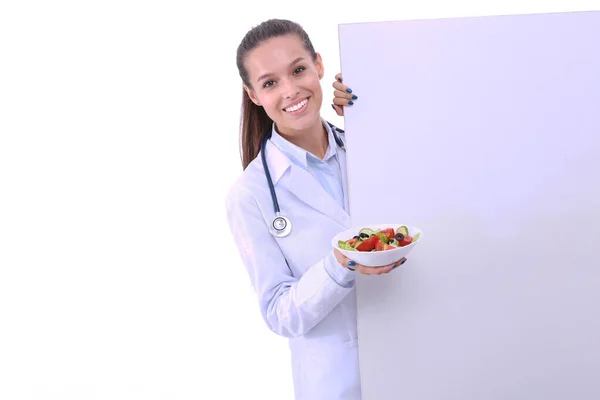 Портрет красивой женщины-врача, держащей тарелку со свежими овощами, стоящими рядом с пустым местом. Женщины-врачи — стоковое фото