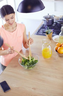Gülümseyen genç kadın mutfakta taze salata karıştırıyor..