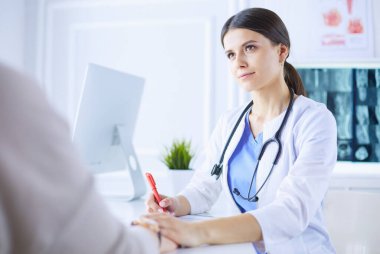 Kadın doktor hastane danışma odasında bir hastayı sakinleştiriyor, elini tutuyor.