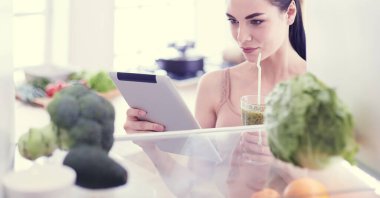 Mutfaktaki masada bir bardak lezzetli, sağlıklı smoothie ile genç bir kadın.