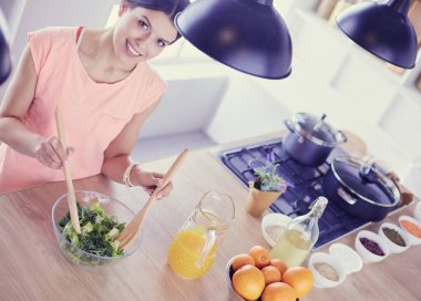 Gülümseyen genç kadın mutfakta taze salata karıştırıyor..