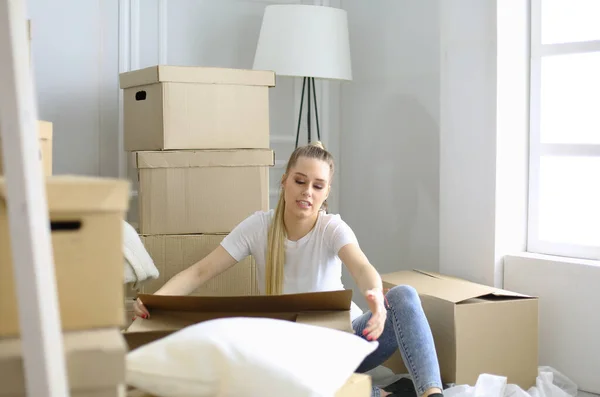 Een mooie alleenstaande jonge vrouw die dozen uitpakt en naar een nieuw huis verhuist. Een vrouw kijkt naar hier tablet — Stockfoto