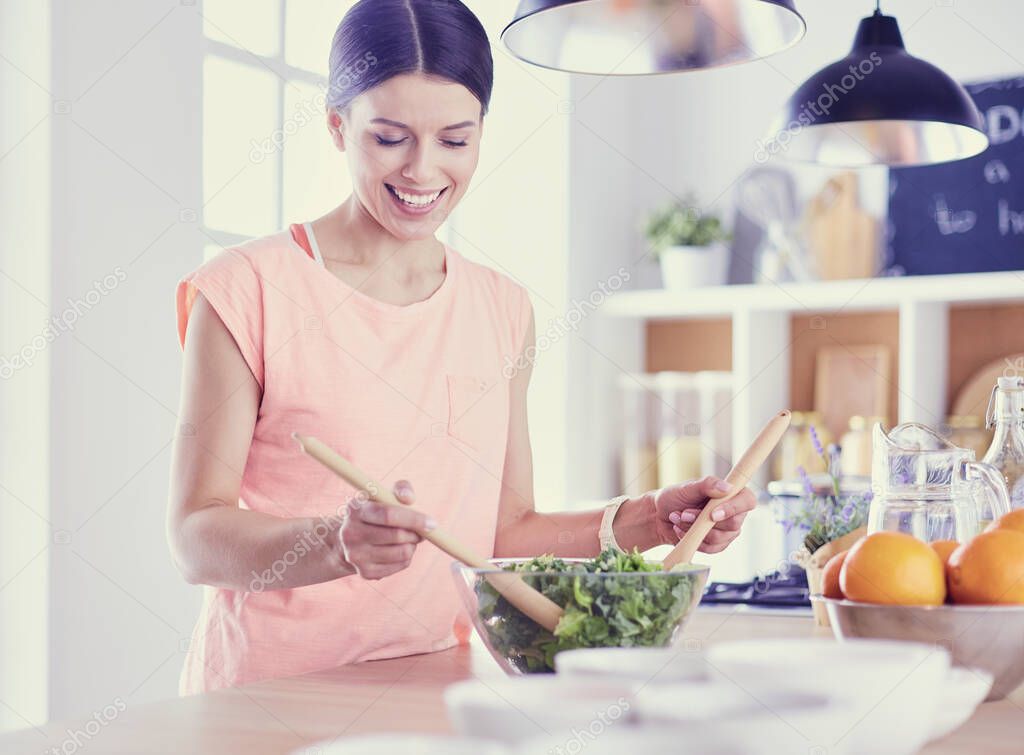 Smiling young woman mixing fresh salad in the kitchen.