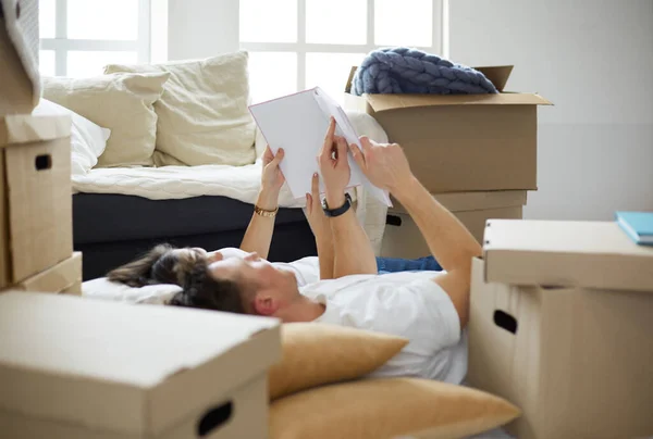 Leuk stel dat kartonnen dozen uitpakt in hun nieuwe huis, liggend op de vloer en kijkend naar een familiealbum — Stockfoto