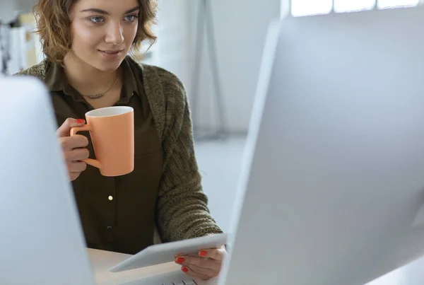 Mulher atraente sentado na mesa do escritório, segurando uma xícara de café — Fotografia de Stock