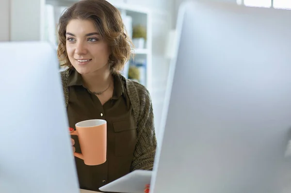 Mulher atraente sentado na mesa do escritório, segurando uma xícara de café — Fotografia de Stock