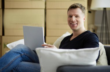 Yeni eve taşınan mutlu genç adamın portresi. Kollarında dijital tablet tutan bir adam.