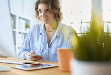 Evdeki bir masada birden fazla cihaz kullanarak çalışan mutlu kadın.