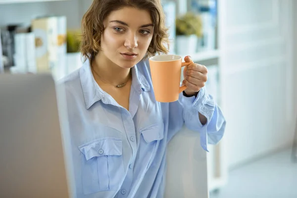 Attraktiv kvinna som sitter vid skrivbordet och håller en kopp kaffe — Stockfoto