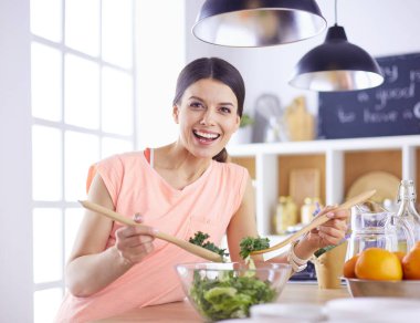 Gülümseyen genç kadın mutfakta taze salata karıştırıyor..