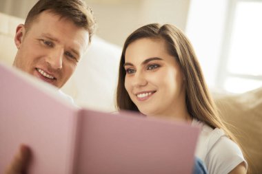 Yeni evlerinde karton kutuları açan sevimli bir çift yerde oturuyor ve bir aile albümüne bakıyor.