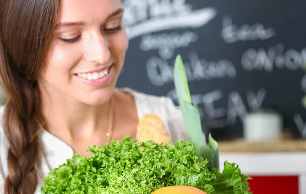 Mujer joven sonriente sosteniendo verduras de pie en la cocina. Jovencita sonriente —  Fotos de Stock